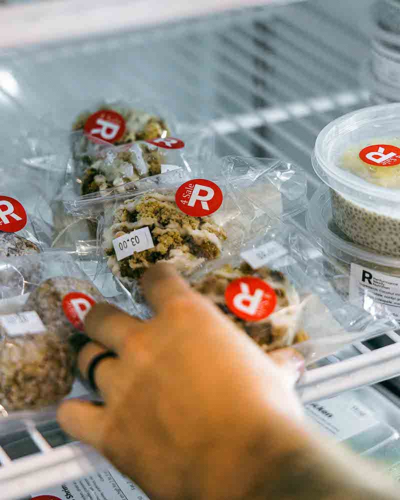 Hand reaching into a refrigerated display of packaged food items with red