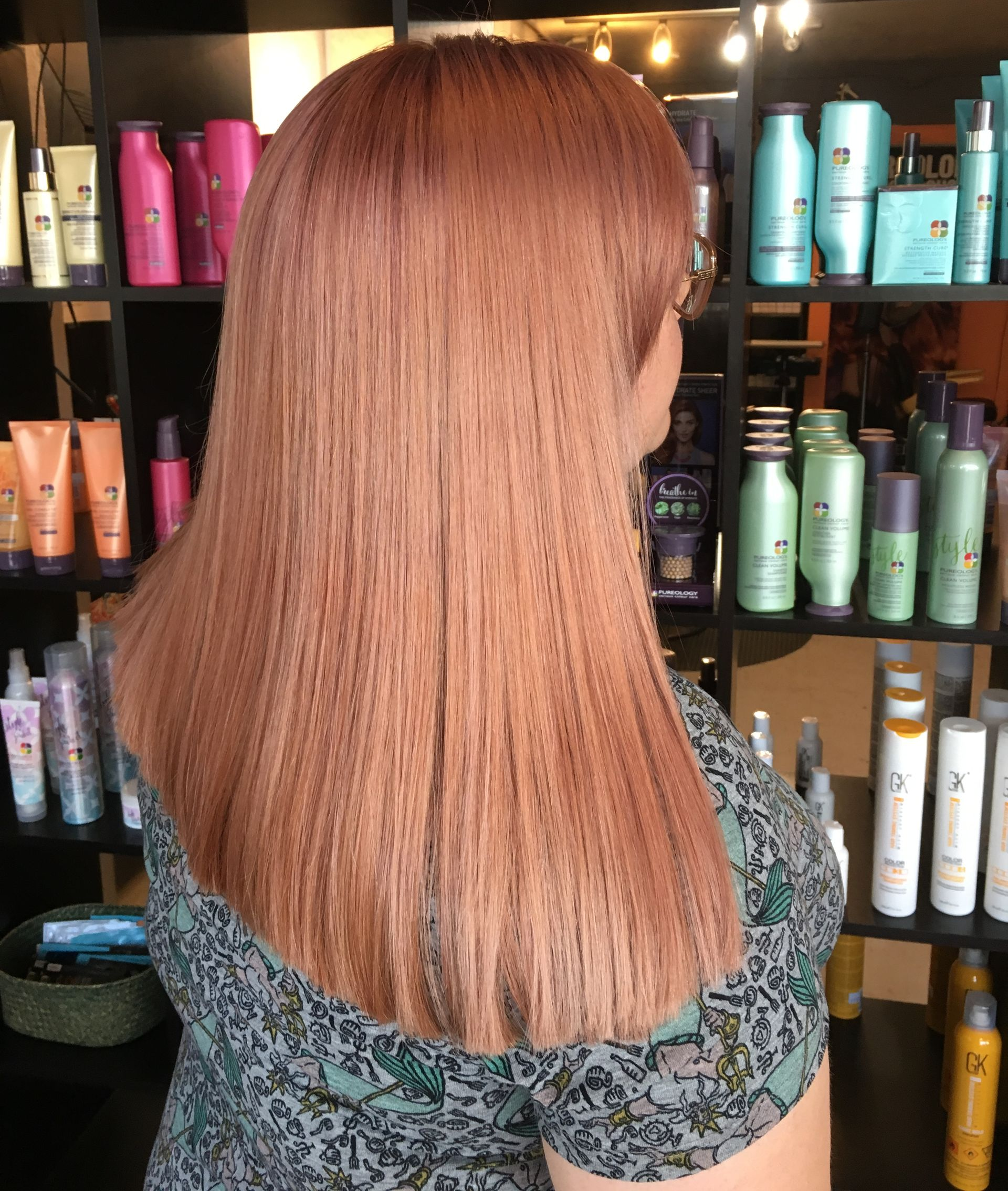 A person with crimped, copper-toned hair seen from behind, standing in a hair salon with products on shelves behind them.