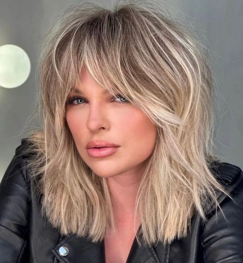 Shoulder-length blonde hair with long, face-framing layered bangs and a textured, messy finish.
