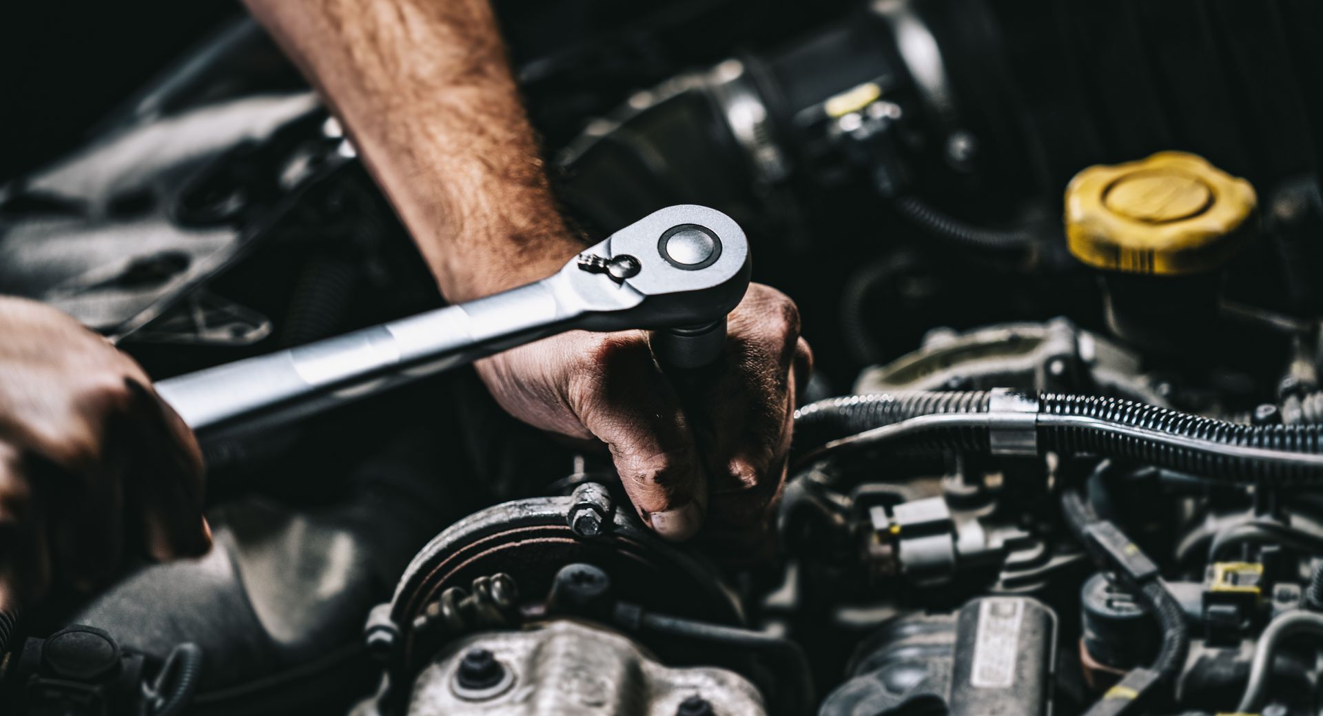 A man is working on a car engine with a wrench. | Halton Auto Service & Transmission