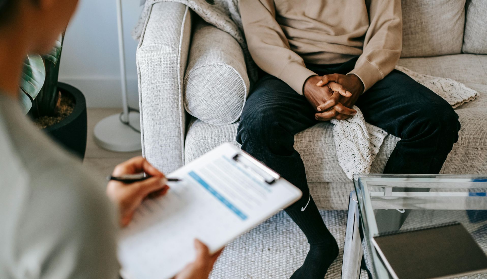 Therapist taking notes during a counseling session with a seated client in a living room.