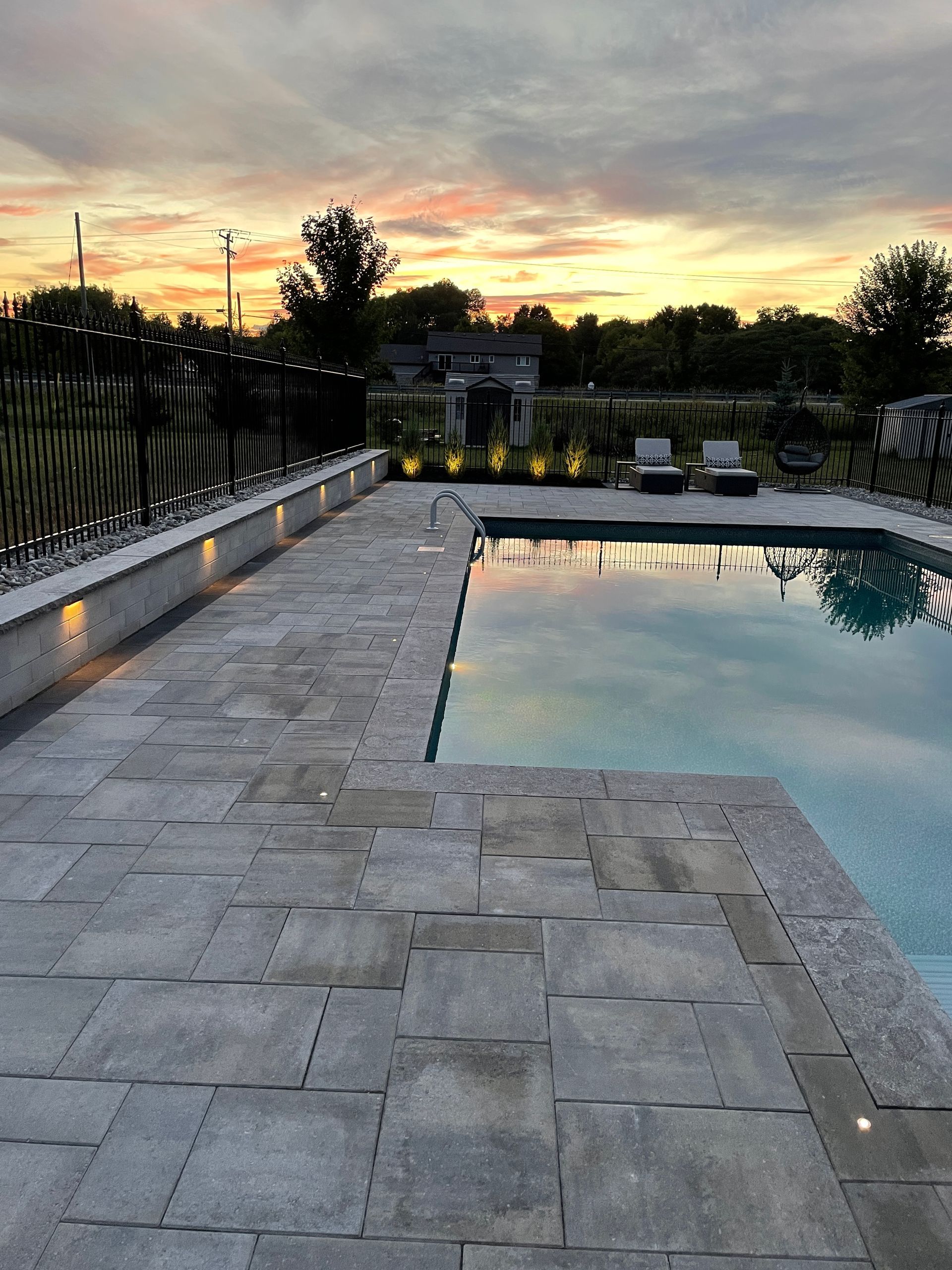 Pool area at dusk with gray patio, pool, and sunset sky.