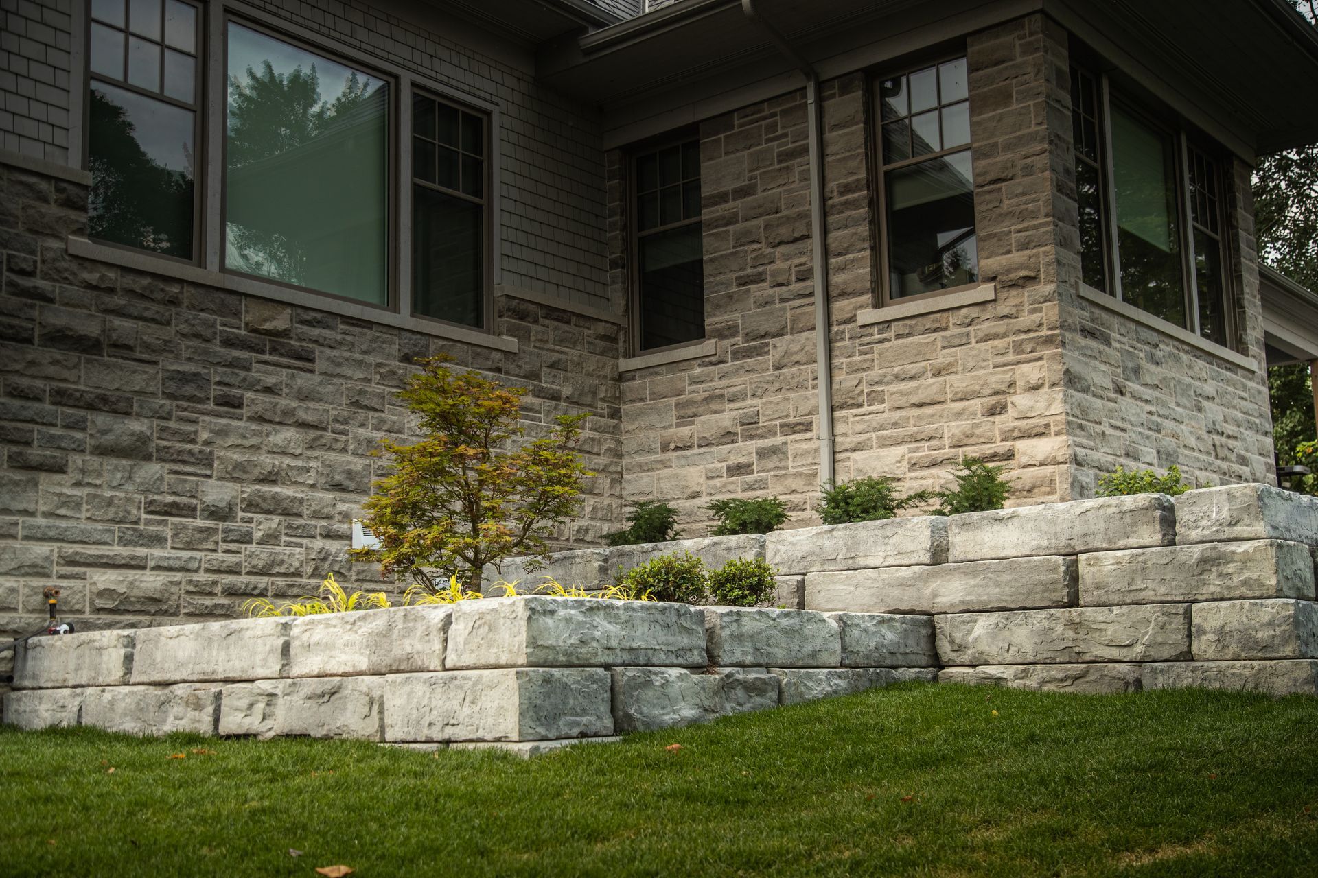 Stone facade and tiered retaining wall with small plants on green lawn.