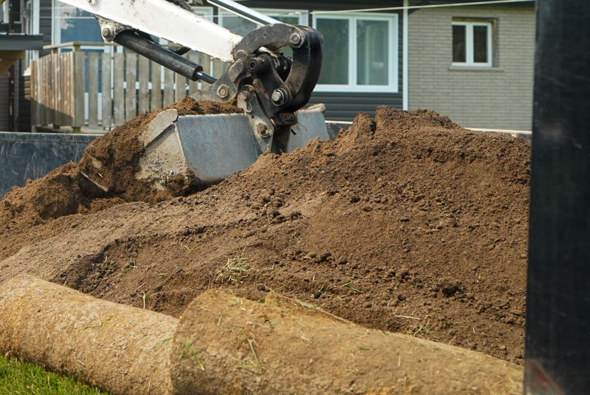 Excavator preparing and grading soil for a residential landscaping project before hardscape.
