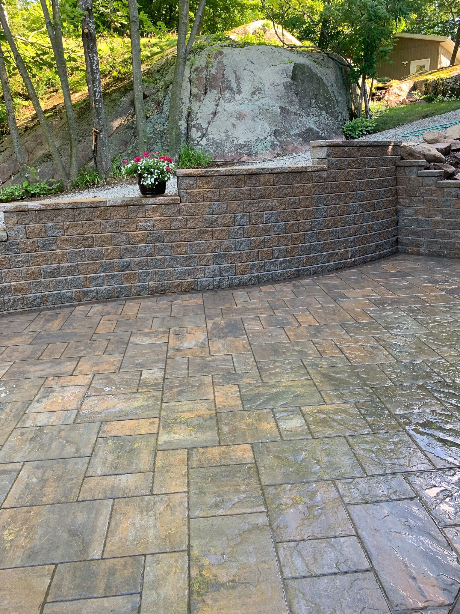 Stone patio with brick wall and large boulder in the background; a potted plant sits atop the wall.