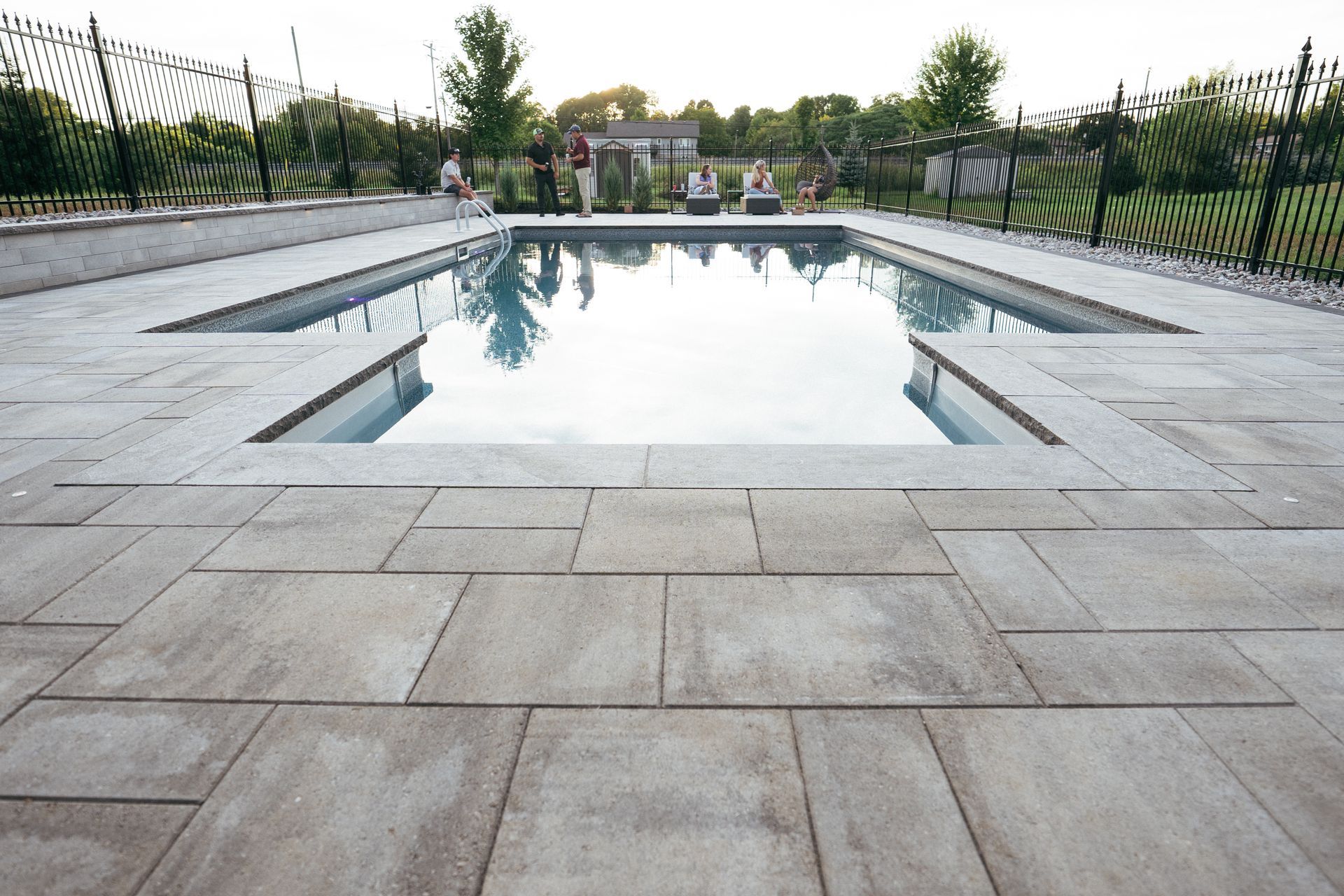 A rectangular in-ground pool surrounded by gray stone patio. People are visible in the background.