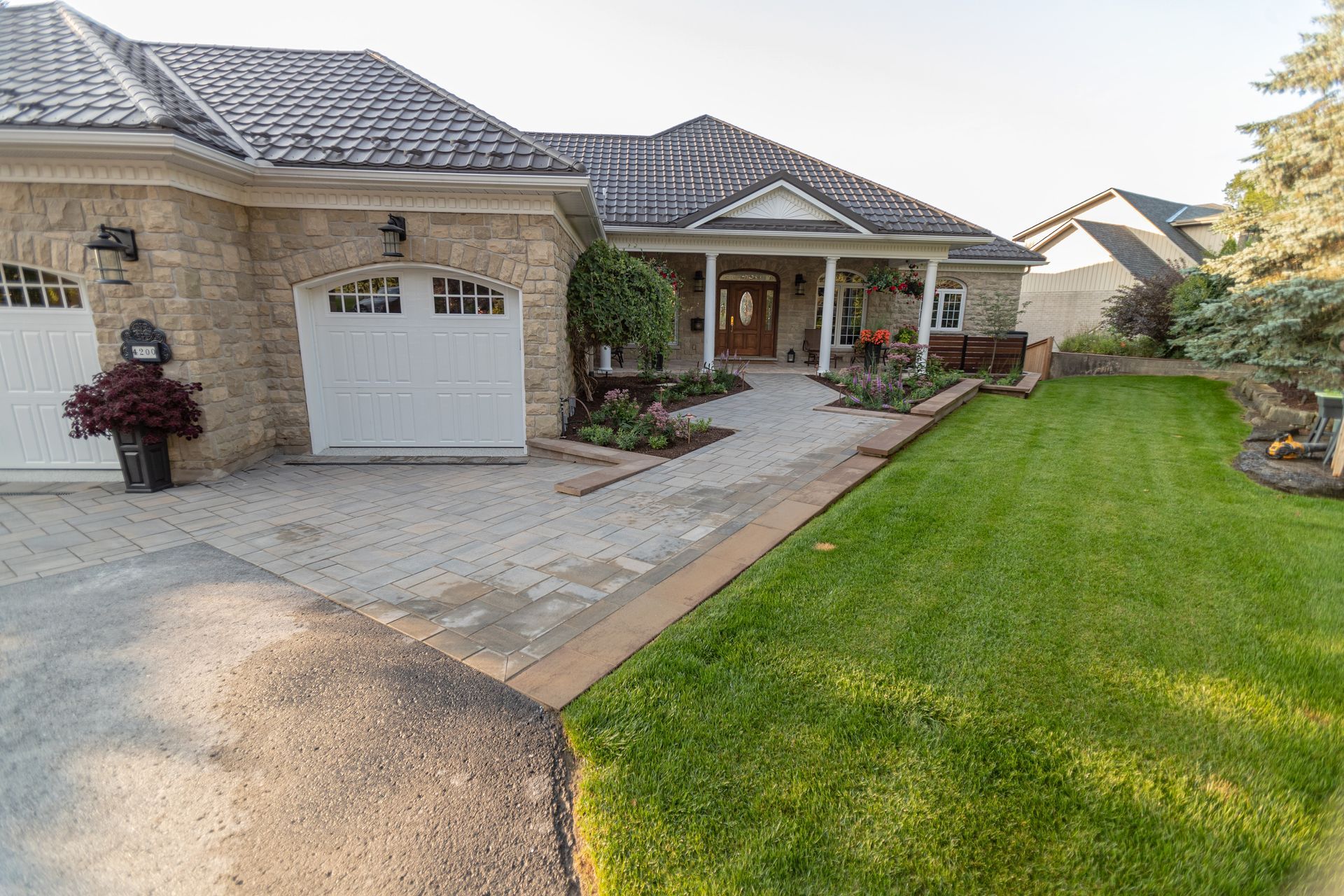 Stone house with white garage doors, walkway to the entrance, and well-manicured lawn.