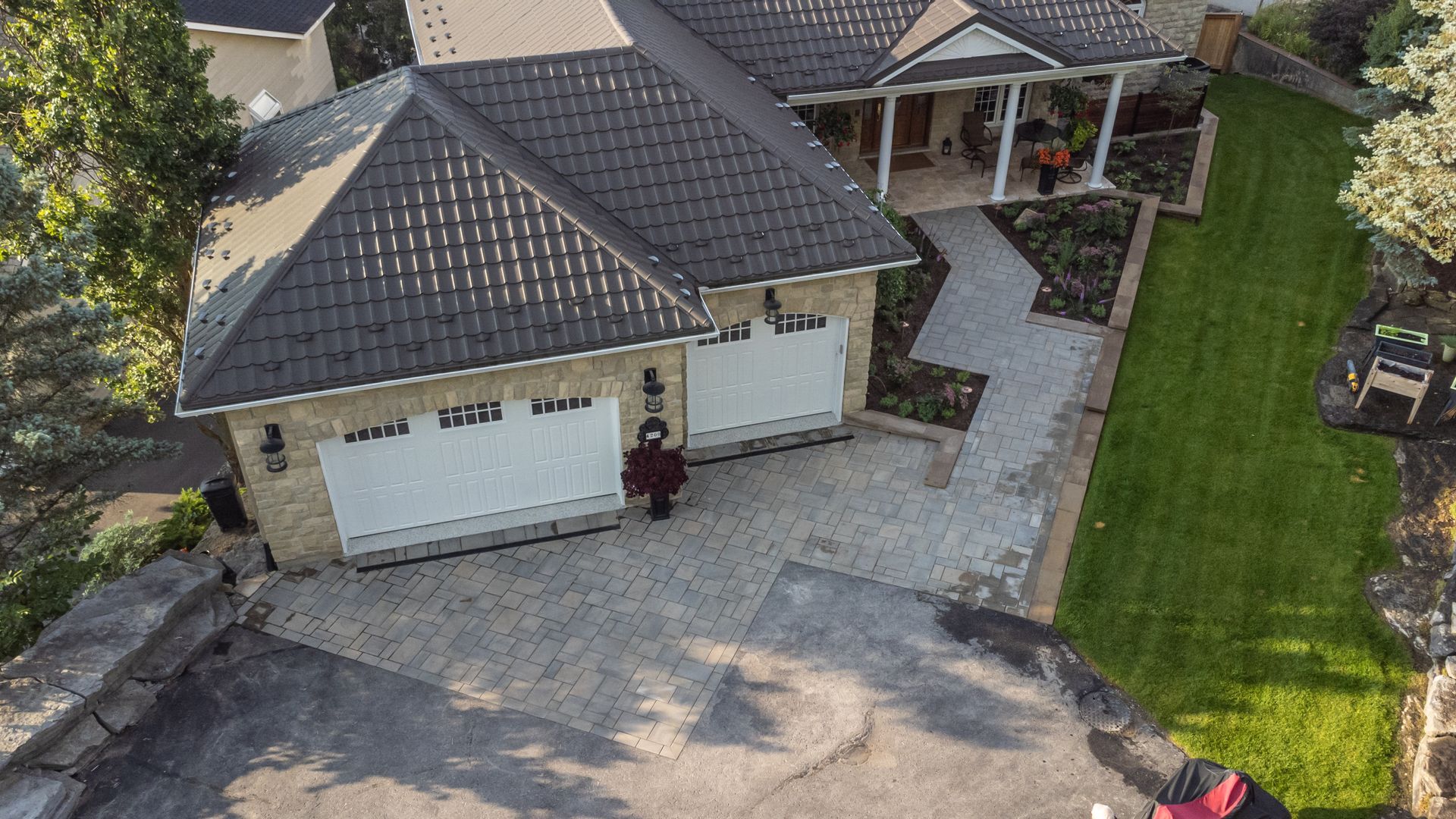 Stone house with two-car garage, manicured lawn, and paved driveway.