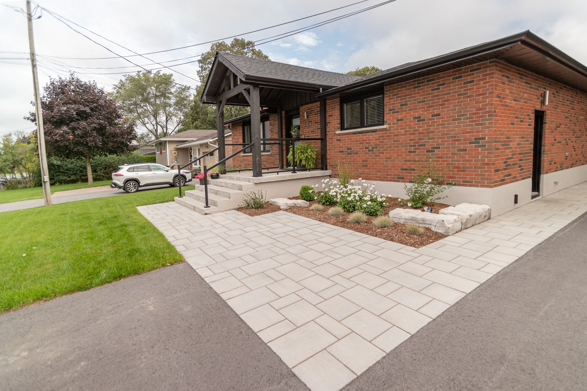 Brick house with paved entrance and landscaped garden. A car parked on the street.