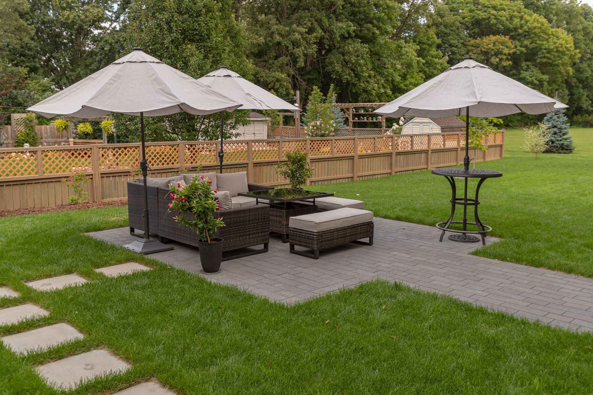 Modern backyard patio with outdoor seating, umbrellas, stone pavers, and landscaped lawn.