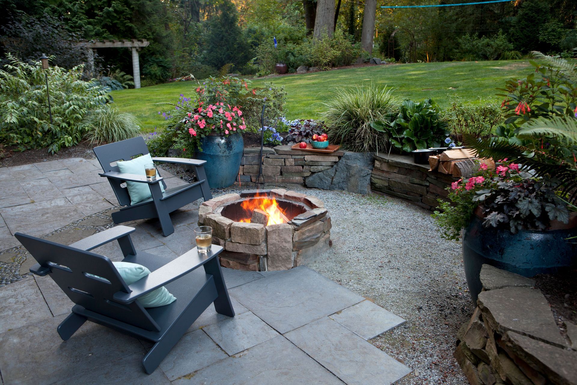 Professionally designed backyard patio with a stone fire pit, seating area, and retaining wall.