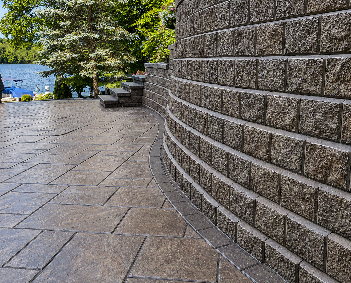 Curved concrete block retaining wall beside a stamped stone patio overlooking a lake.