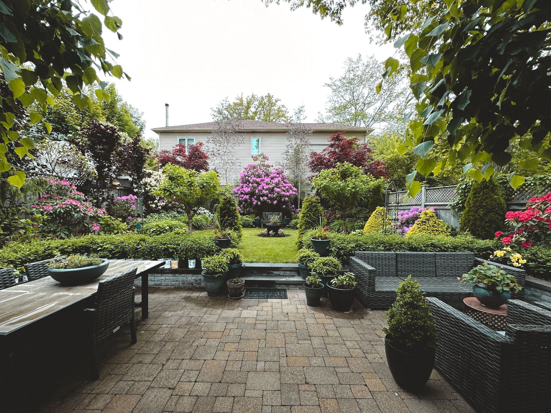 Private backyard patio surrounded by trees, shrubs, and garden beds.