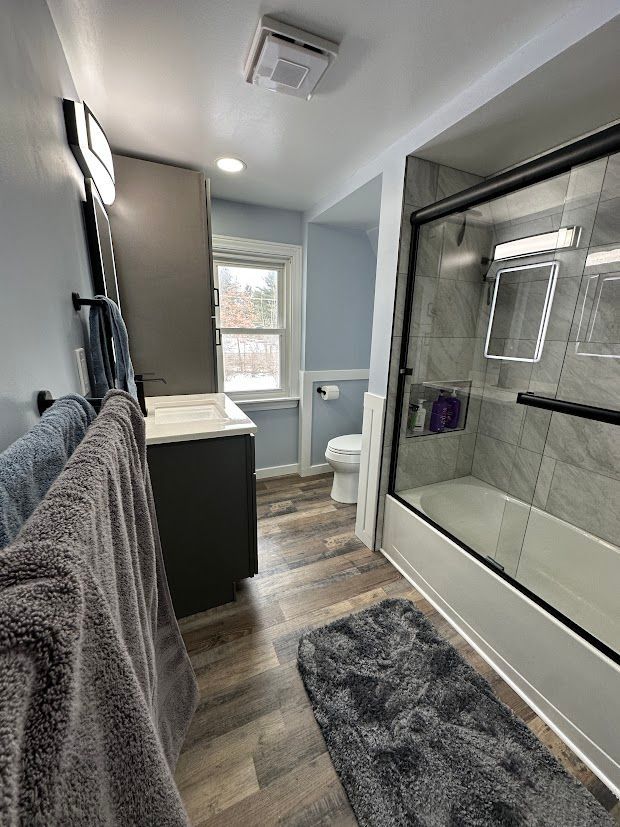 Bathroom with gray walls, wood-look floor, shower with glass door, dark vanity, and window.