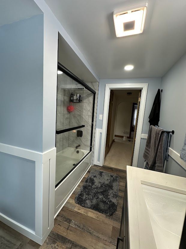 Bathroom with blue walls, white trim, shower with glass door, and wood-look flooring.