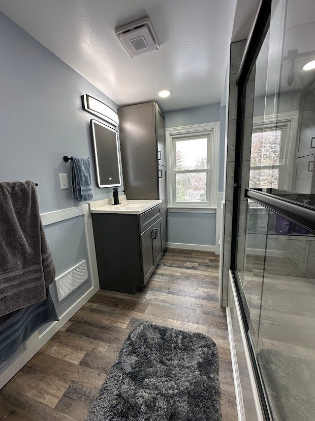Bathroom with blue walls, dark gray vanity, wood-look floor, and glass shower.