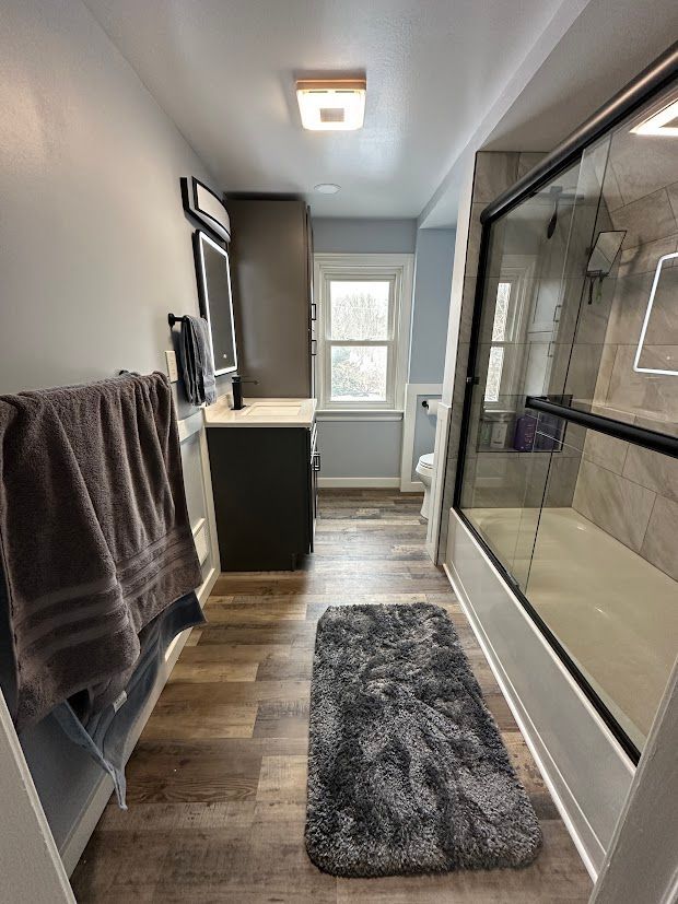 Narrow bathroom with wood-look floor, gray walls, shower with glass door, and dark gray vanity.