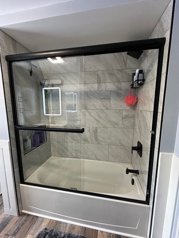Bathroom with a sliding glass shower door and black trim; gray tiled walls.