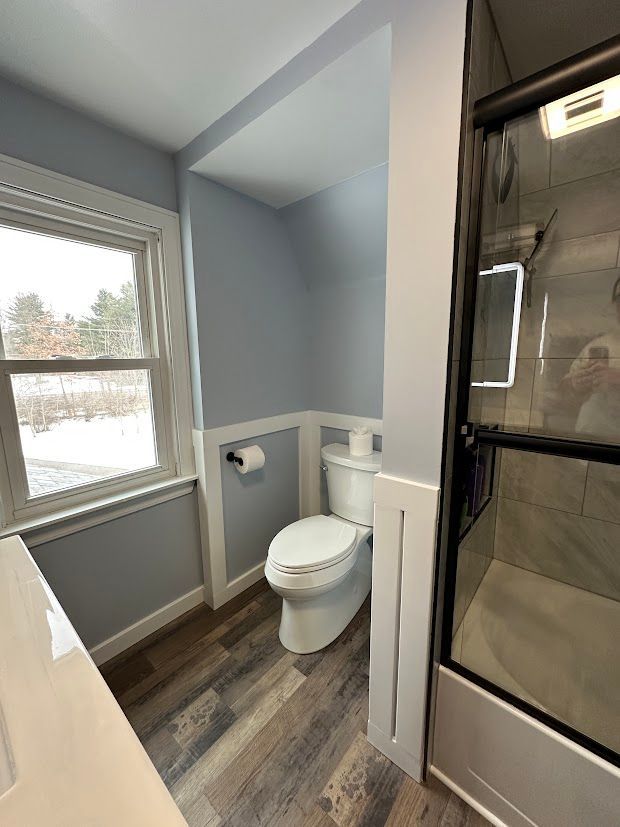 Bathroom with a white toilet, blue walls, a window, and a glass shower door.