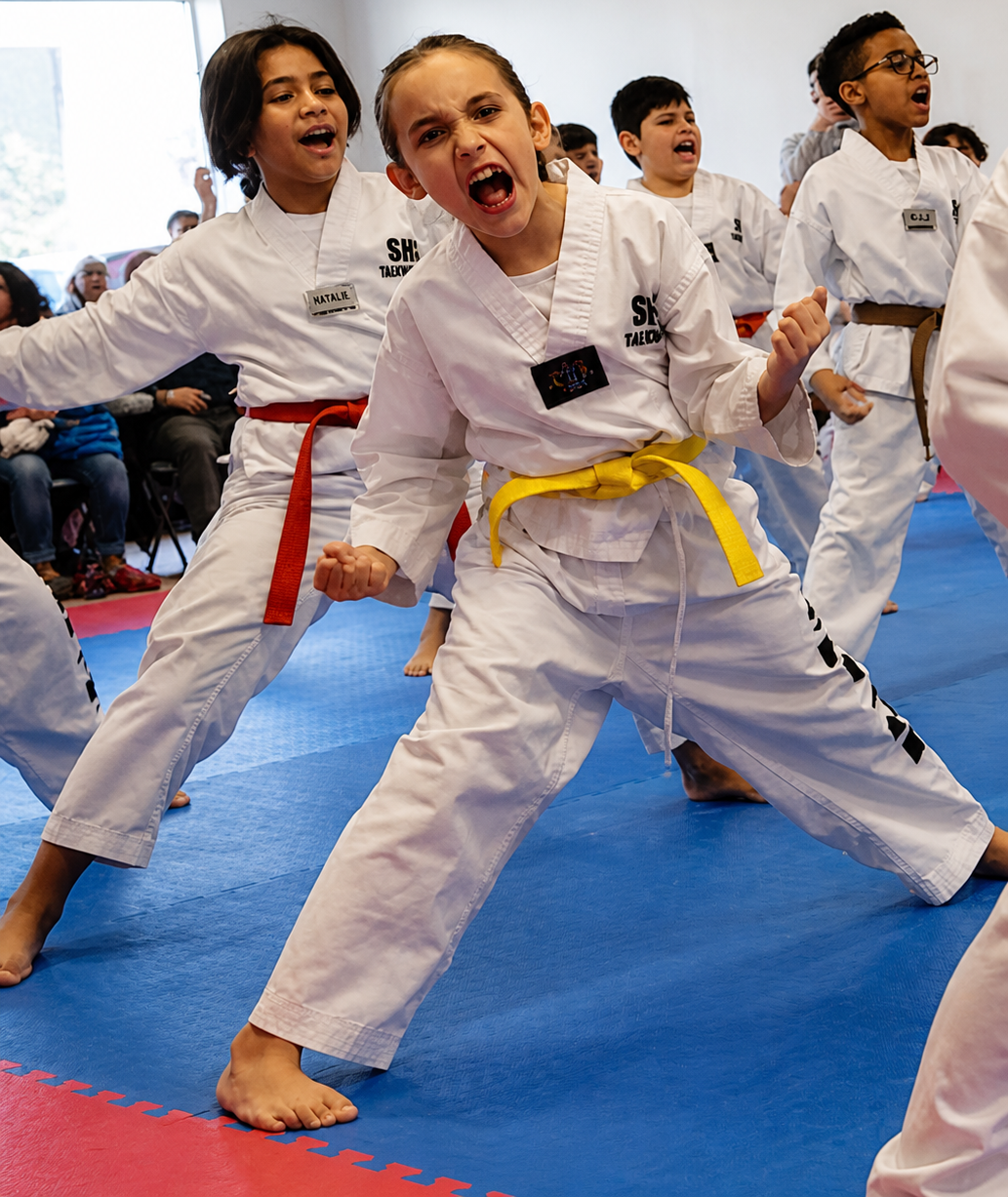 Two people grappling on a mat, one in a black gi, the other in a rash guard, legs entangled.