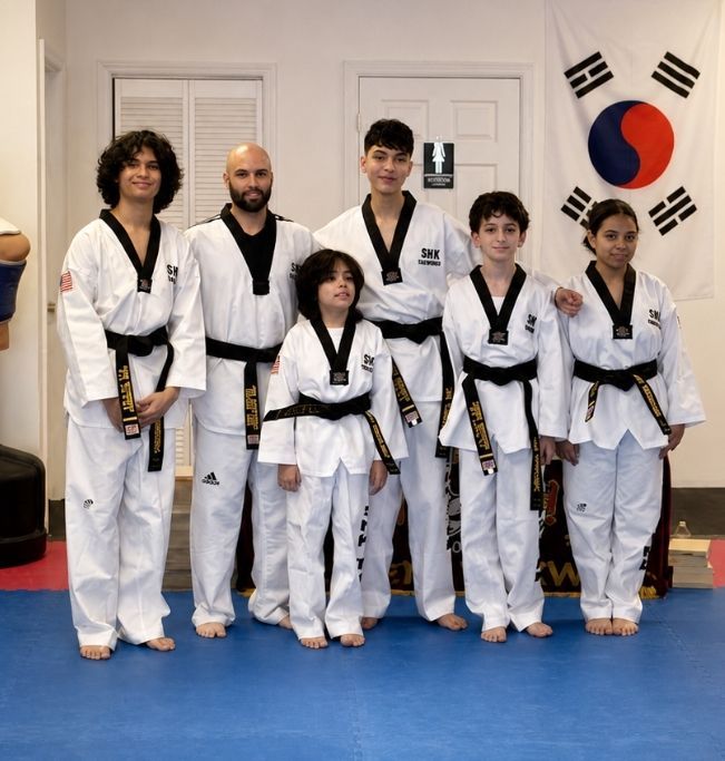 Two children practicing Brazilian Jiu-Jitsu on a mat. One child in white gi has the other in a leg lock. A girl watches.