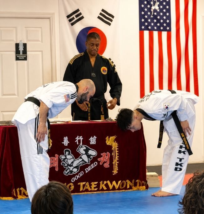 Five people in jiu-jitsu gear pose together in a gym. Smiling, some have arms around each other. Machado logo visible.