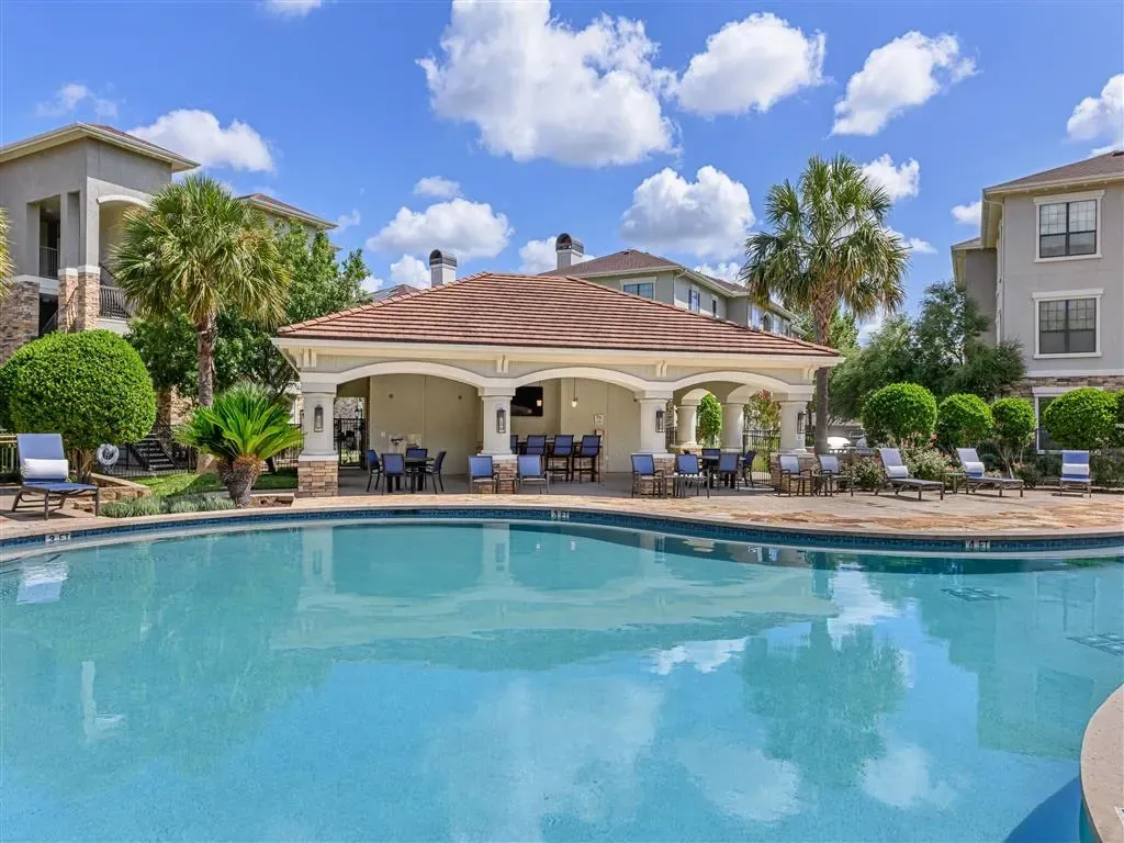 Resort-style swimming pool with lounge chairs and a covered cabana with seating and bar area.