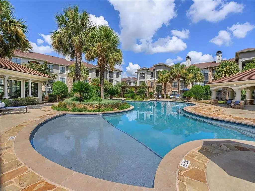 Resort-style pool with palm trees and apartment buildings in the background.