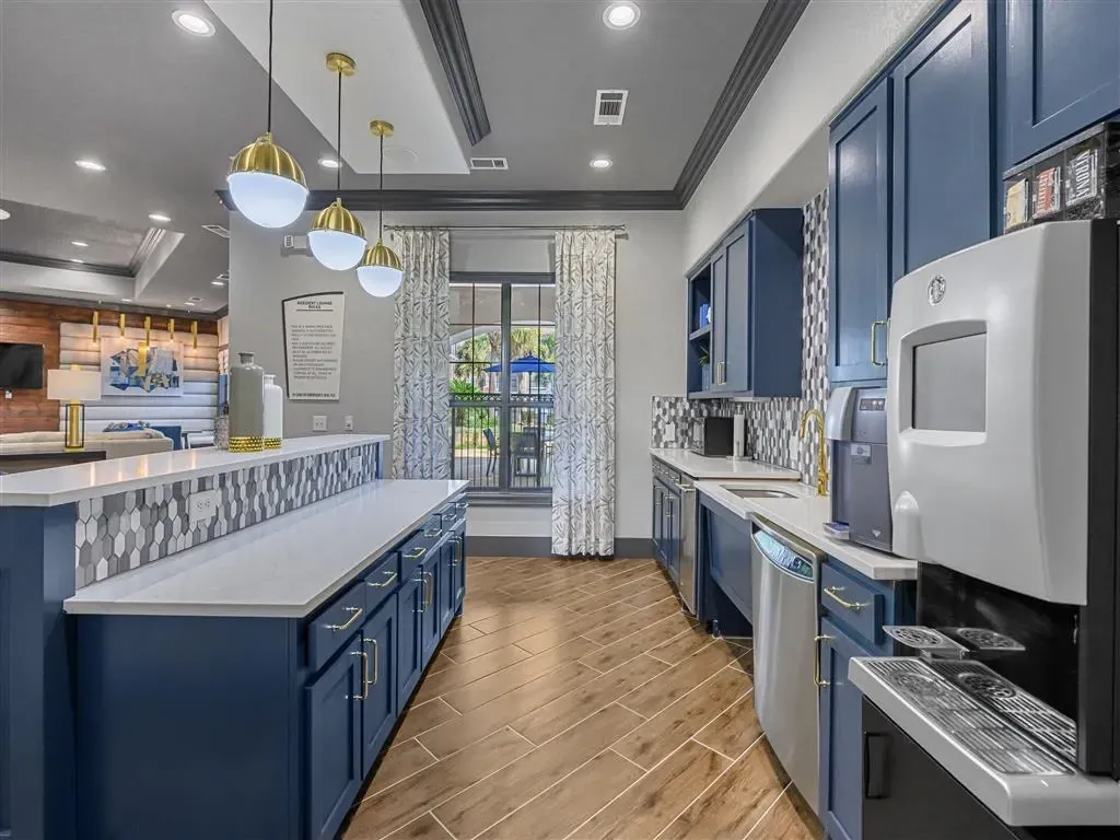 Community lounge kitchen with blue cabinets, white countertops, and coffee maker.
