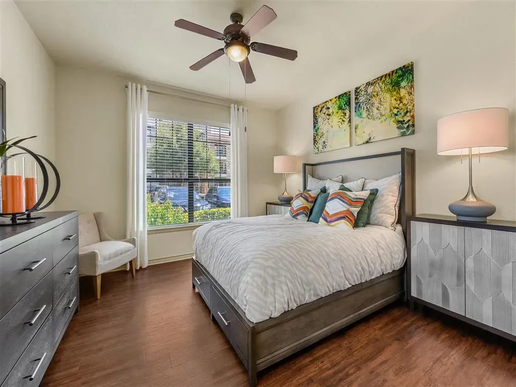 A staged bedroom with a queen-size bed, dresser, nightstands, and a ceiling fan.