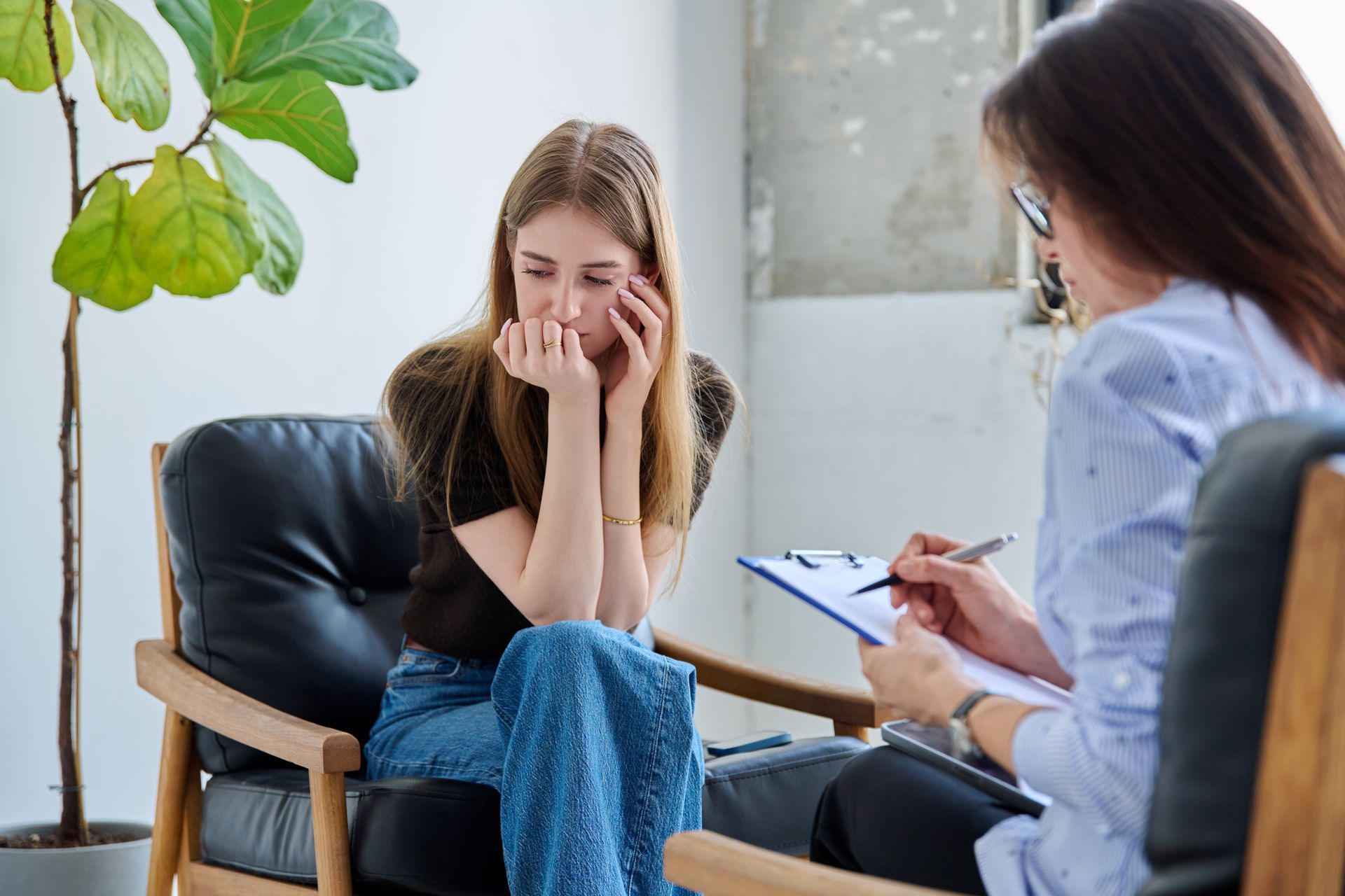 Two people in a counseling session, one crying while the other takes notes.