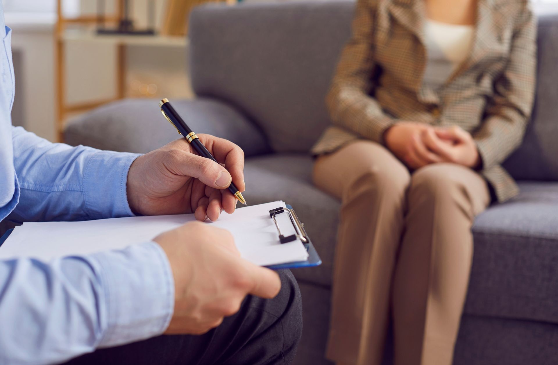 Therapist taking notes during a counseling session with a seated client on a sofa