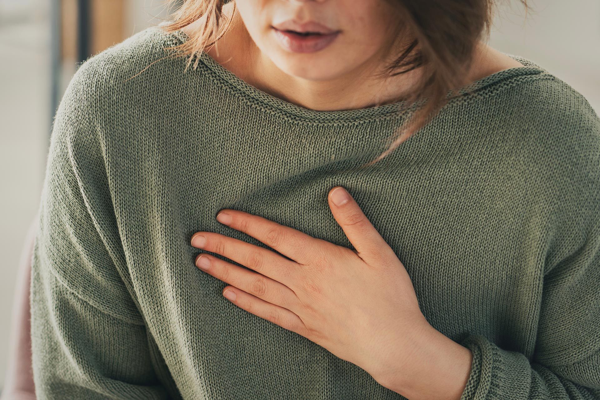 Person in a green sweater holding a hand to their chest, showing a close-up of discomfort. Person in a green sweater holding a hand to their chest, showing a close-up of discomfort.