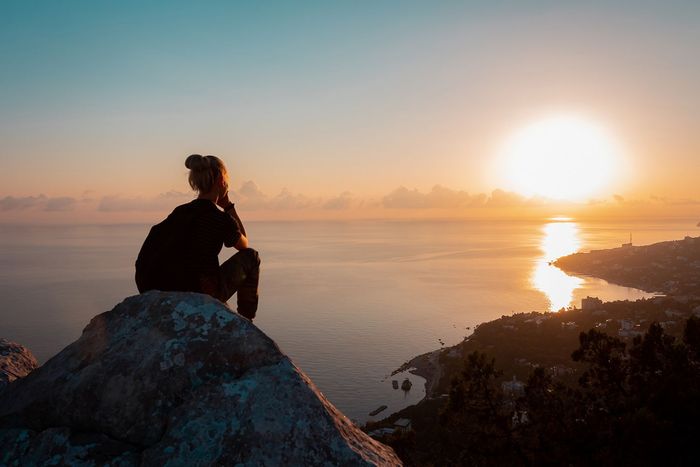 Woman on Top of Mountain — Laguna Hills, CA — Dr. Debra A Hill, MD Woman seated on a rock overlooking ocean, watching sunset. Sun casts golden light; silhouette.
