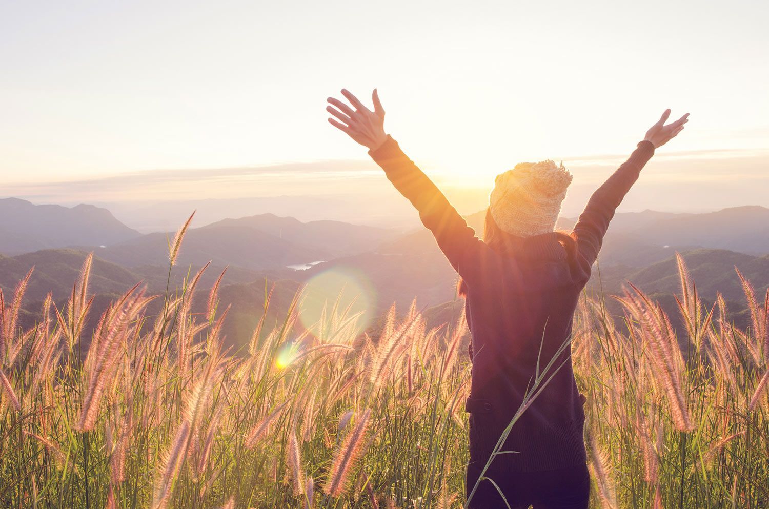 Woman Enjoying the Sunset — Laguna Hills, CA — Dr. Debra A Hill, MD Woman with arms raised, silhouetted against a sunrise over a field of tall grass.