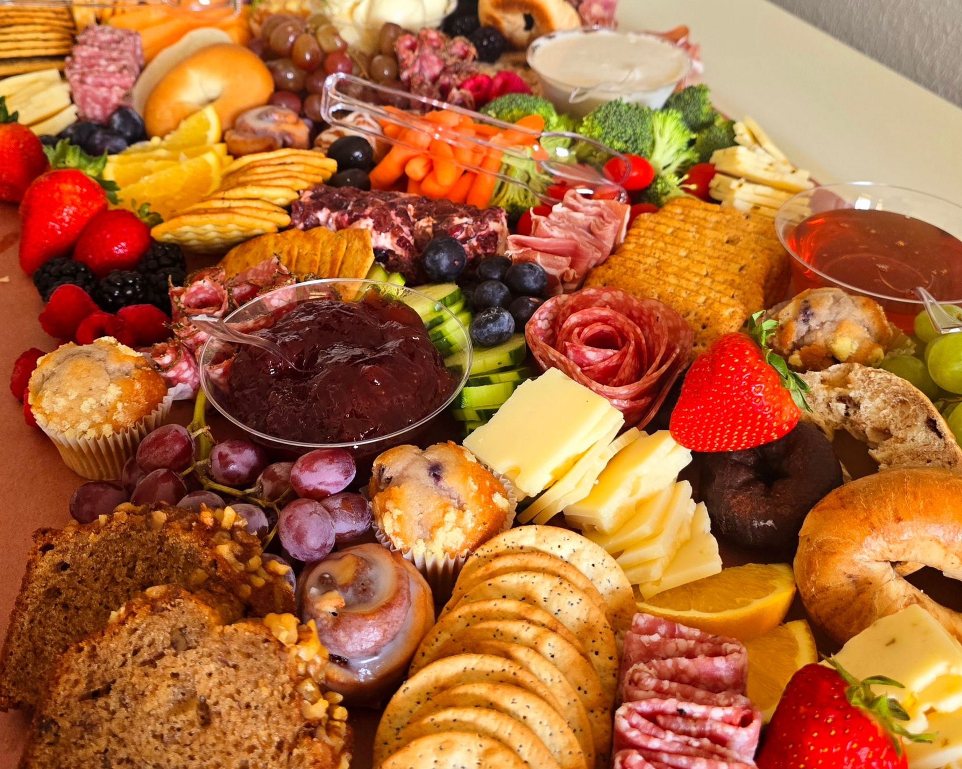 Charcuterie board: colorful assortment of meats, cheeses, fruits, crackers, and dips arranged on a white surface.