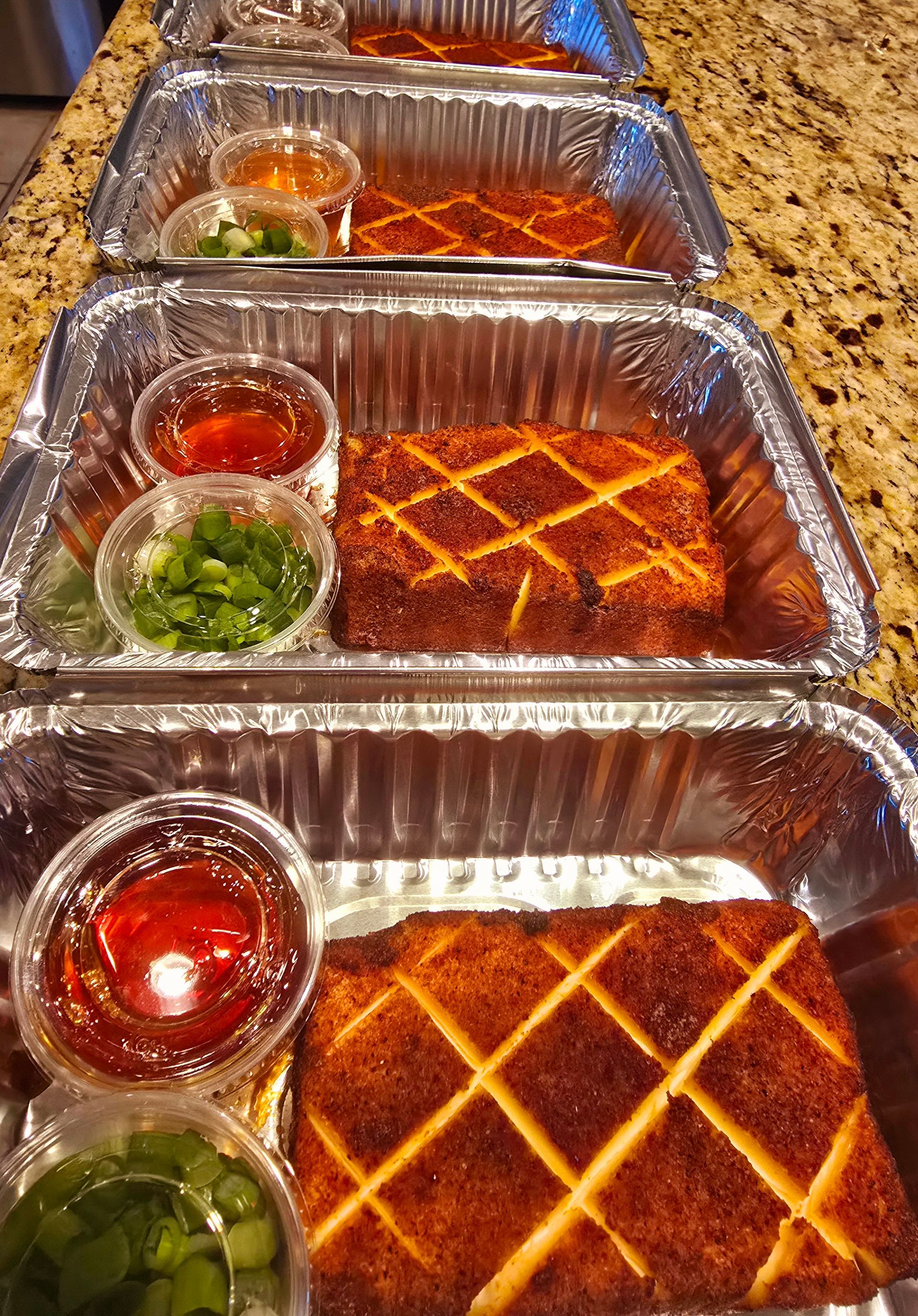 Four takeout containers with fried tofu, dipping sauce, and scallions, on a kitchen counter.