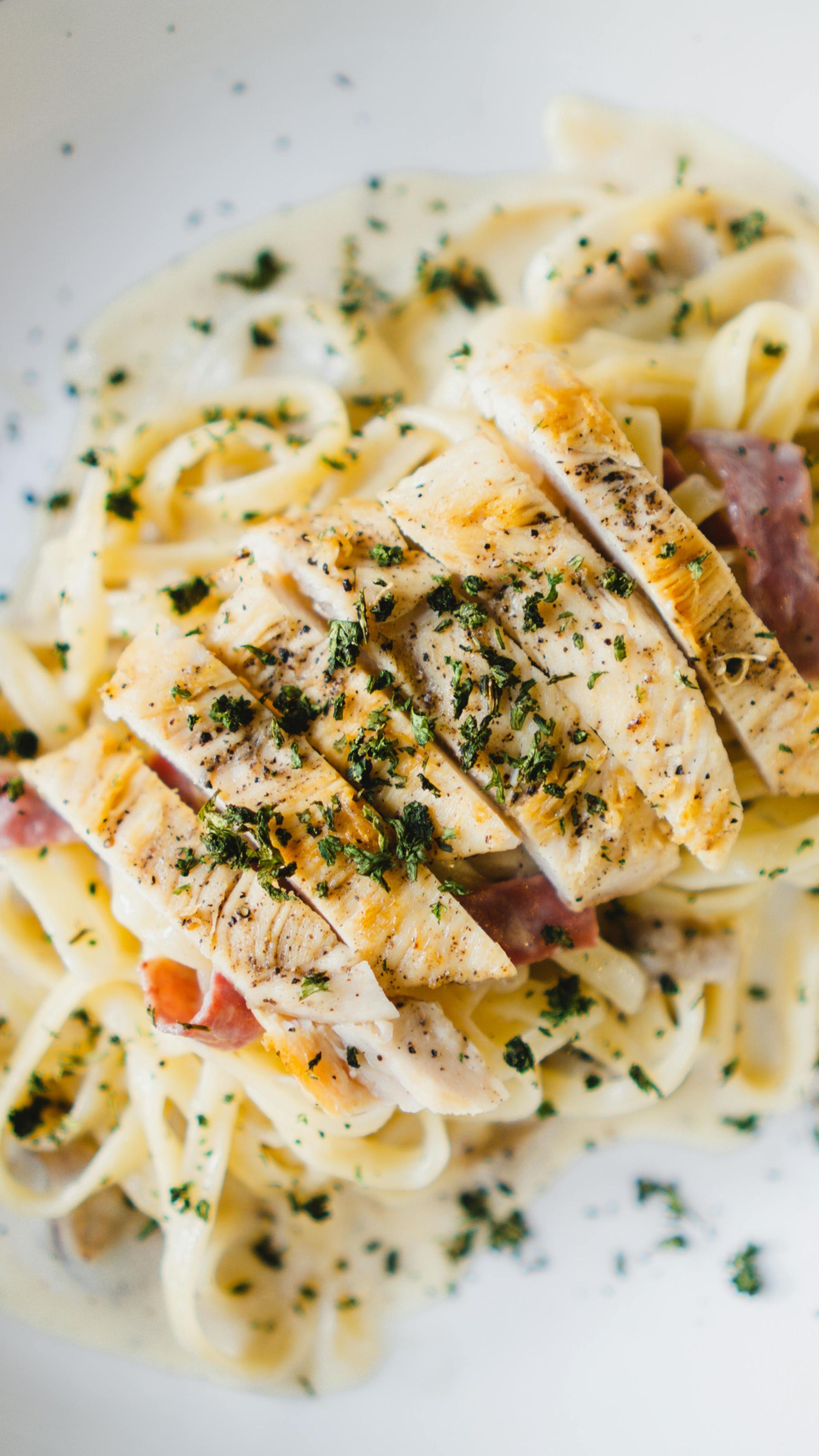 Fettuccine Alfredo with grilled, sliced chicken and parsley garnish.