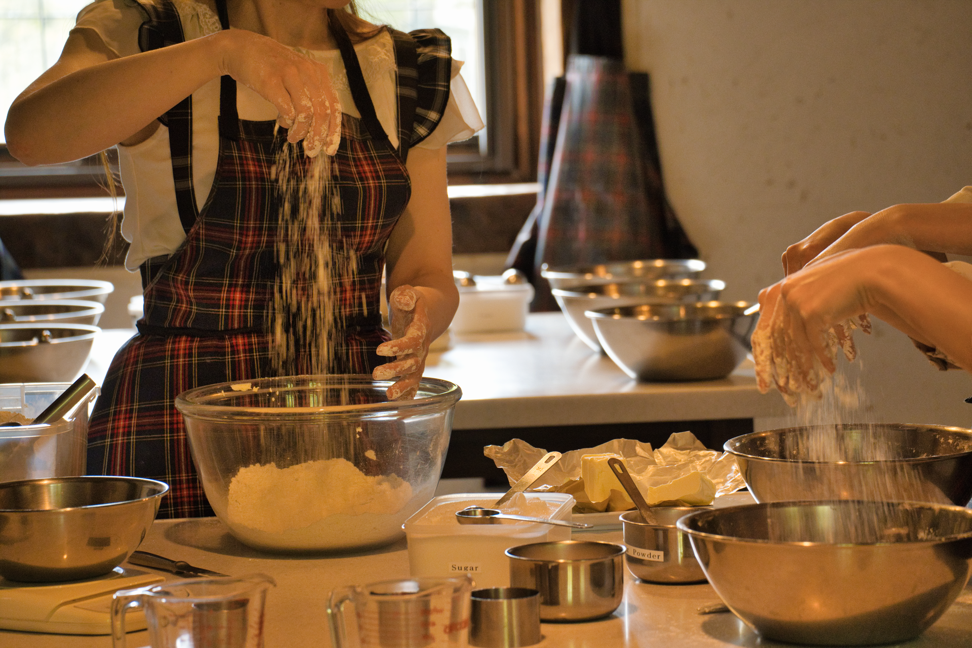 People preparing food on a kitchen counter with bowls, flour, and baking ingredients