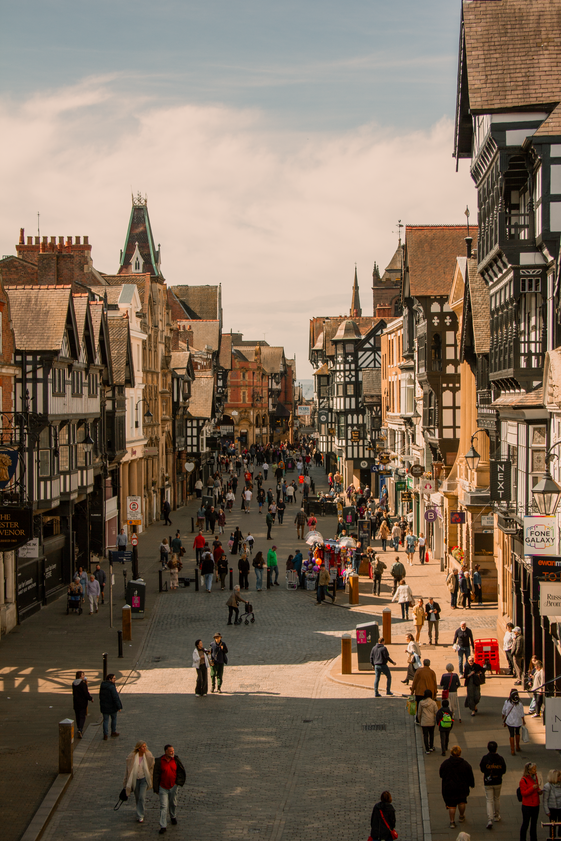 Crowded historic street with cobblestone road and tall timber-framed buildings in warm sunlight