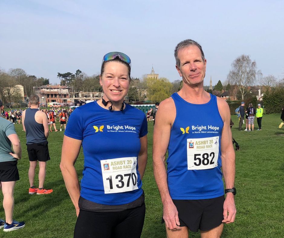 Two runners in blue Bright Vibe shirts posing on a grassy field before a race, with bib numbers 137 and 582