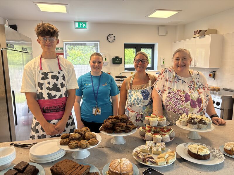 Four people behind a table of baked goods at a community hall event