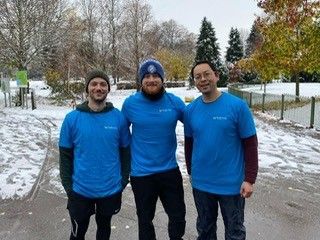 Three people in blue shirts standing on a snowy path outdoors, smiling at the camera.