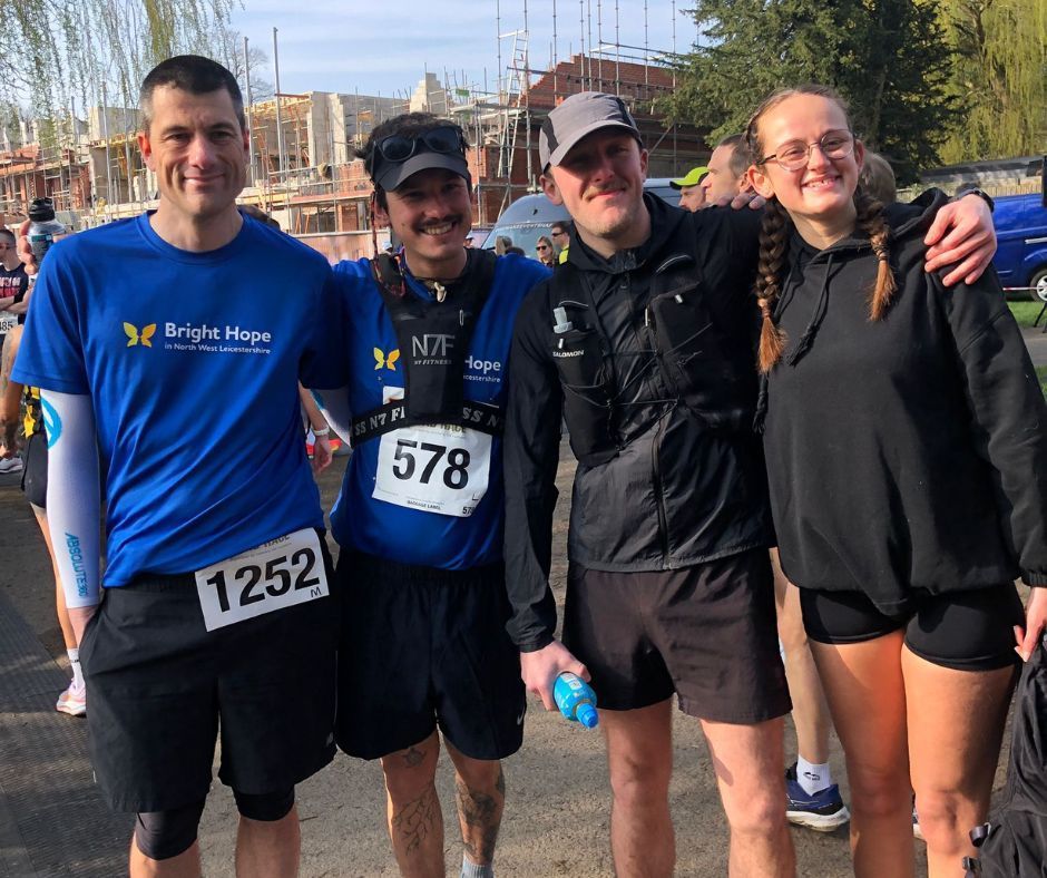 Four runners in blue and black race shirts pose smiling outdoors after a run.