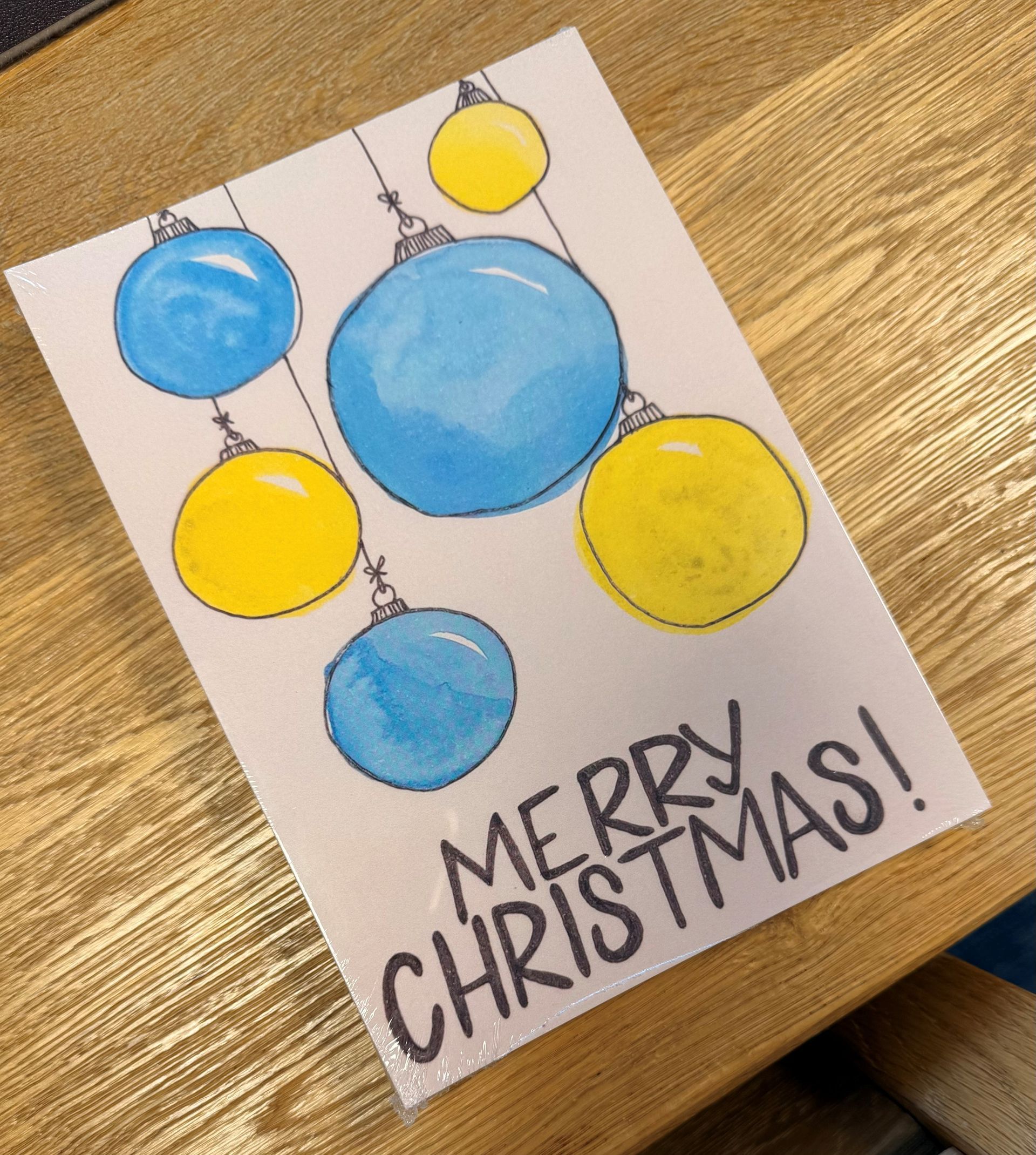 Handmade Christmas card with blue and yellow ornaments and “Merry Christmas!” text