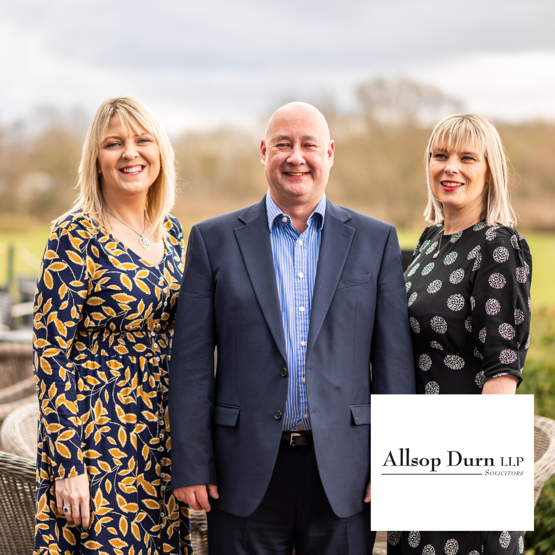 Three people in business attire standing outdoors, smiling, with a law firm logo in the corner