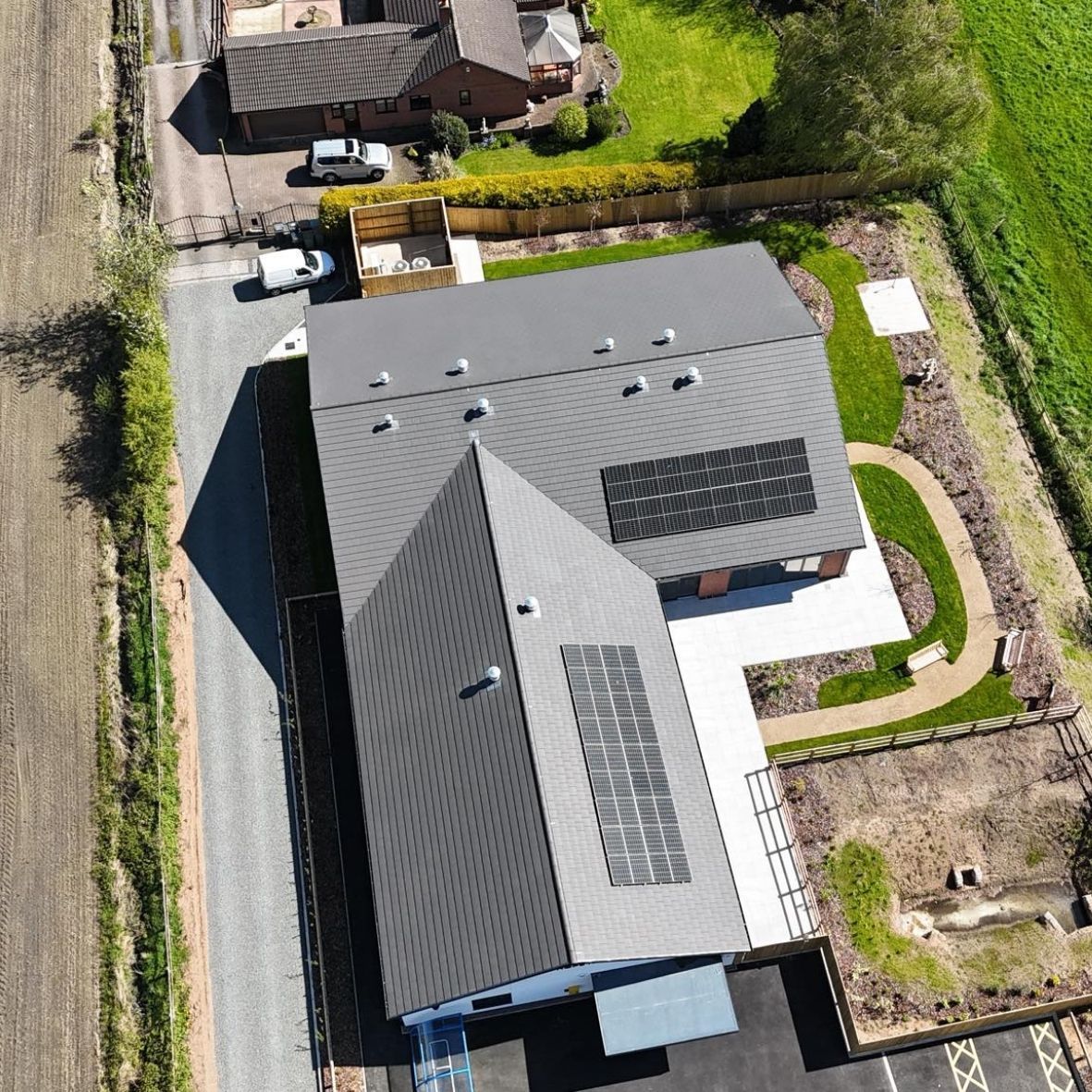 Aerial view of a modern house with a dark roof, solar panels, and a landscaped yard.