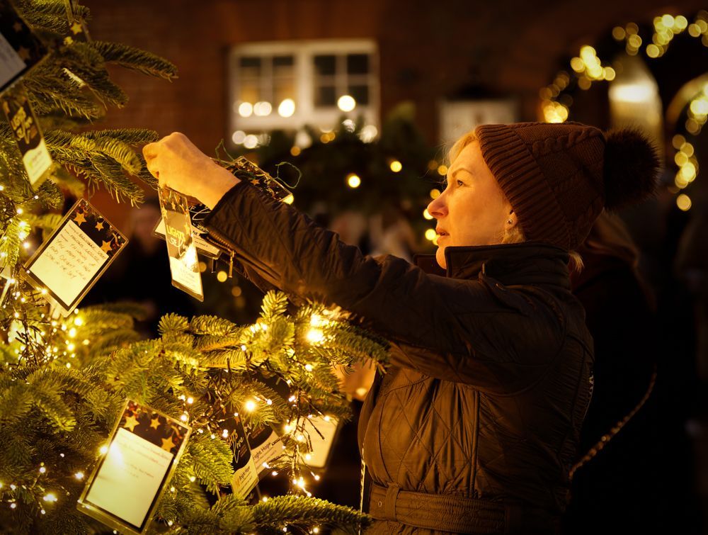 Person hanging lights on an outdoor Christmas tree at night