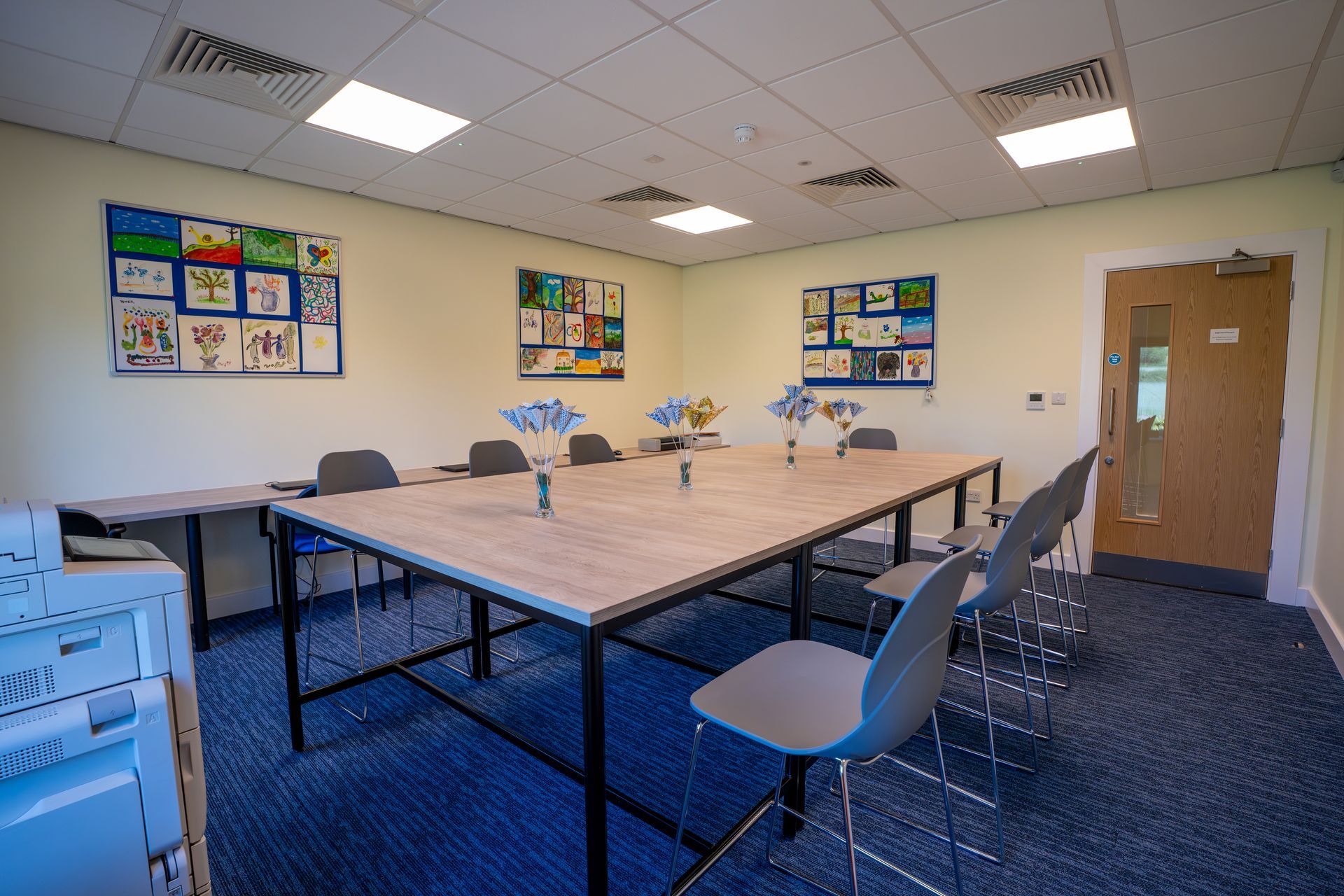 Empty classroom with tables, blue chairs, colorful wall posters, and a wooden door.