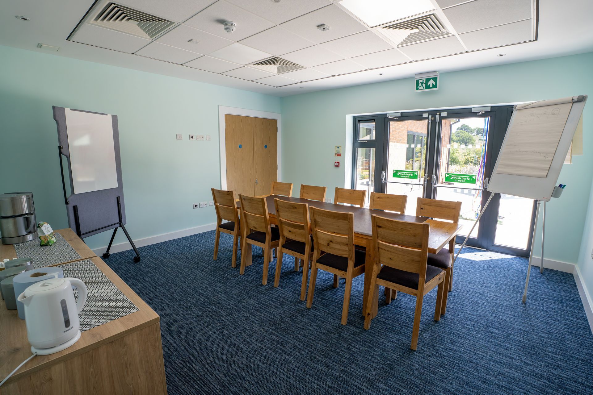 Meeting room with wooden table, blue carpet, and glass doors letting in daylight.